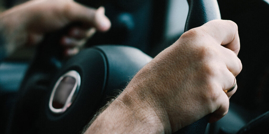 Man holding a car steering wheel, firmly with both hands