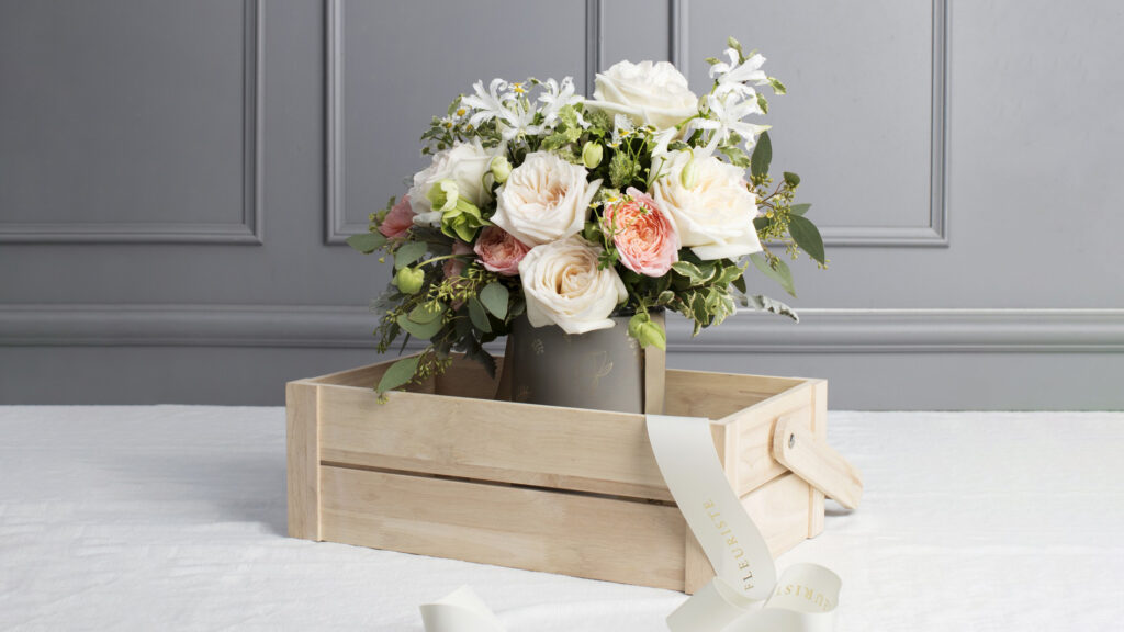 A small bouquet of white and peach roses in a pot standing in a small wooden crate.
