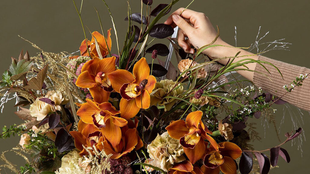 Woman arranging a stunning bouquet of flowers that include beautiful orange orchids.