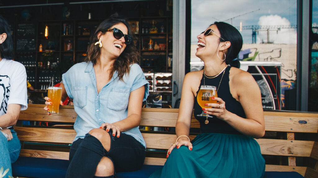 Two women sitting outside drinking beer at a bar.