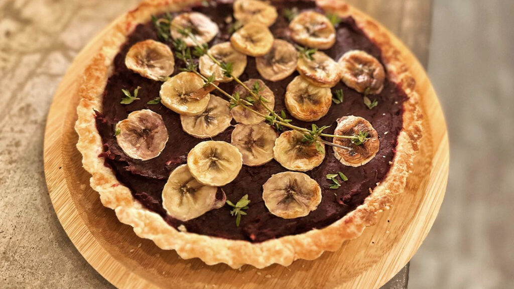 A vegan chocolate tart with dried banana chips on top and sprigs of thyme.