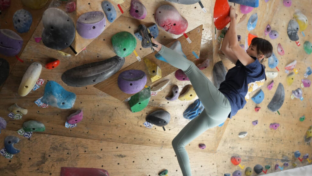 A woman climbs and indoor climbing wall at Keep Climbing Gym.