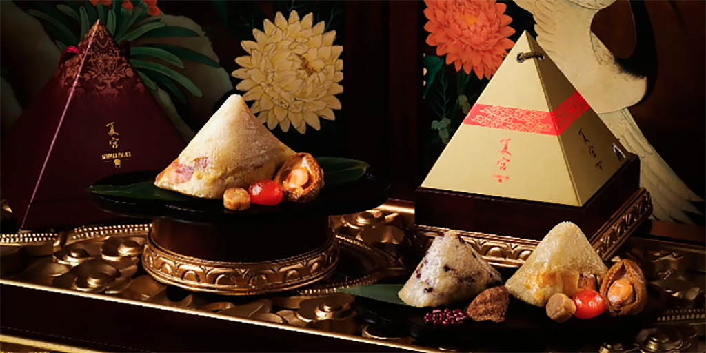 Pyramid rice dumplings next to gold pyramid packaging on a tray.
