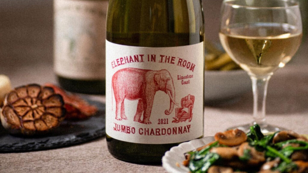 A bottle of wine with an elephant on the label behind a plate of food.