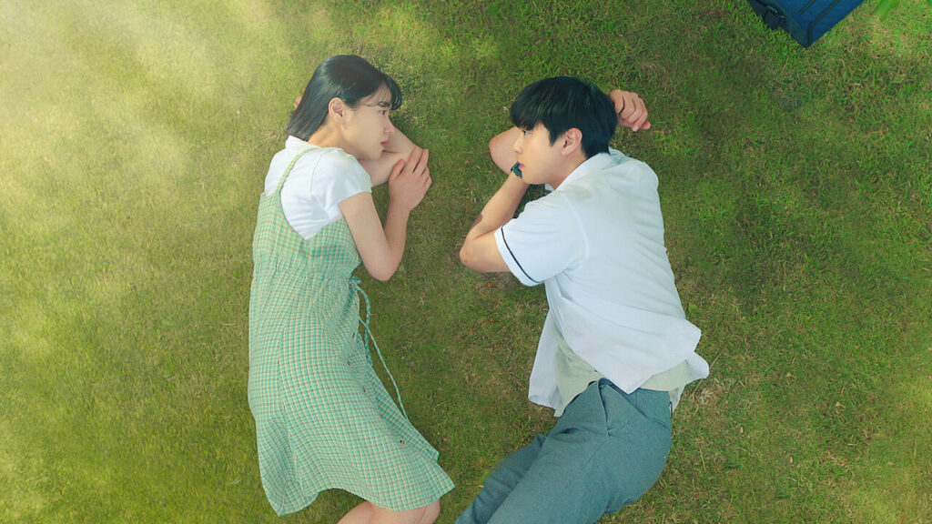 Two people lying on the grass facing each other.