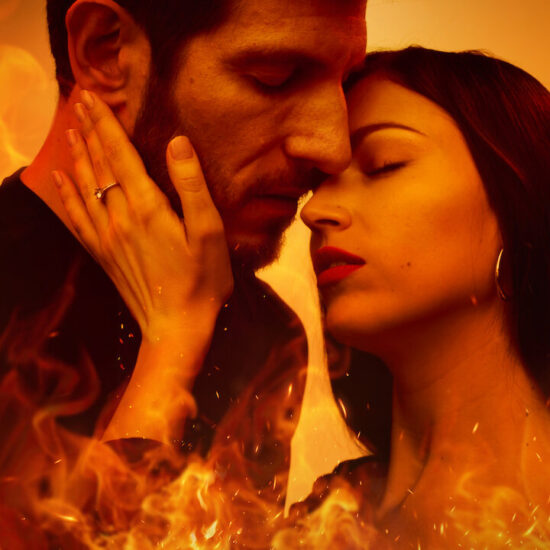 A woman caressing a man's face with flames surrounding them.
