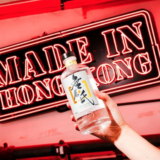 Hand holding a gin bottle in front of a red neon sign that says "Made in Hong Kong"